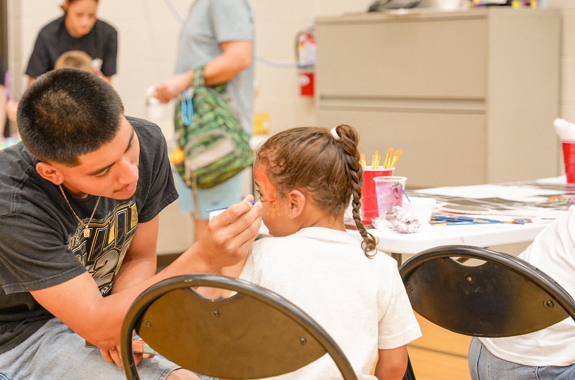 A SOYEP volunteer painting a design on a young girl's face at a community event.